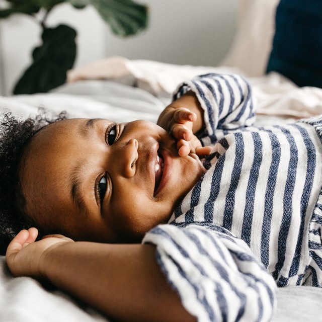 A Cute Little Toddler Girl Laying On The Bed Smiling Image